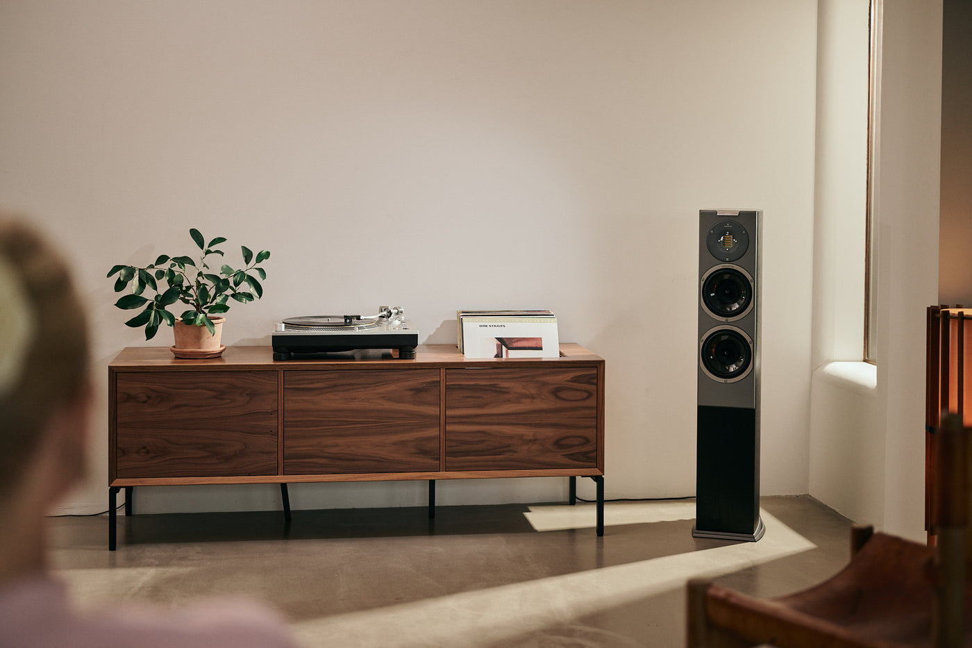 Turntable with Ortofon MC Quintet Black cartridge on a console table next to a loudspeaker. A woman is seated in the foreground, listening to music.